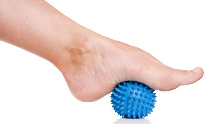 Woman's foot with spiny plastic blue massage ball isolated on white background