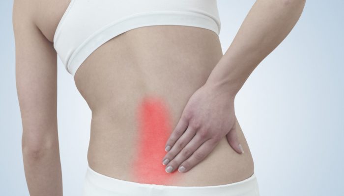 Acute pain in a woman back. Female from behind holding hand to spot of back pain. Concept photo with Color Enhanced blue skin with read spot indicating location of the pain.
