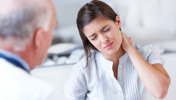 Young woman wincing with pain in a consultation with her doctor - copyspace